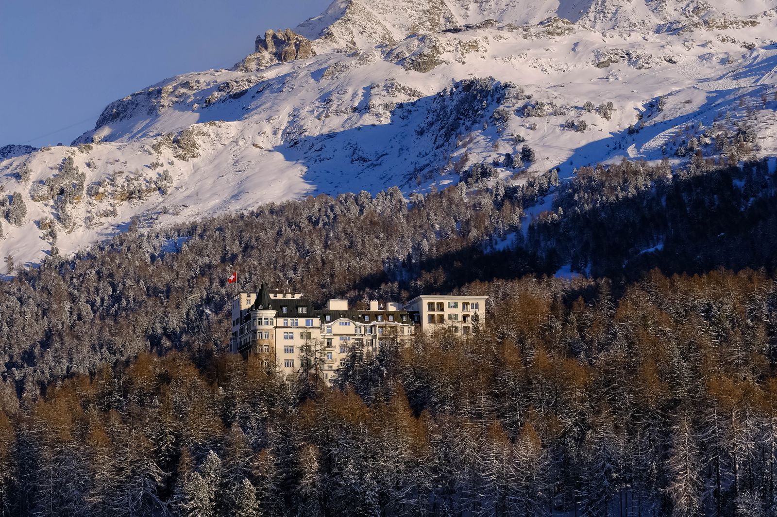 Hotel de montanha entre árvores nevadas, com os Alpes ao fundo
